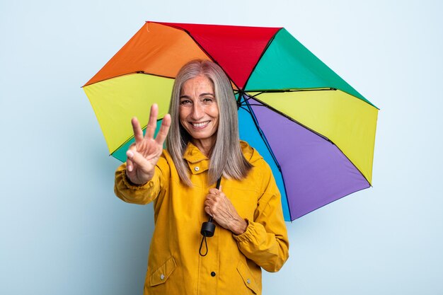 Grijze haarvrouw van middelbare leeftijd die lacht en er vriendelijk uitziet, met nummer drie. paraplu en regenconcept