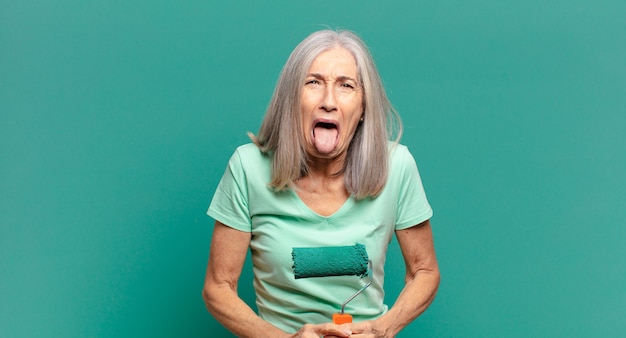 Grijze haarvrouw van middelbare leeftijd met een verfroller die haar muur verfraait