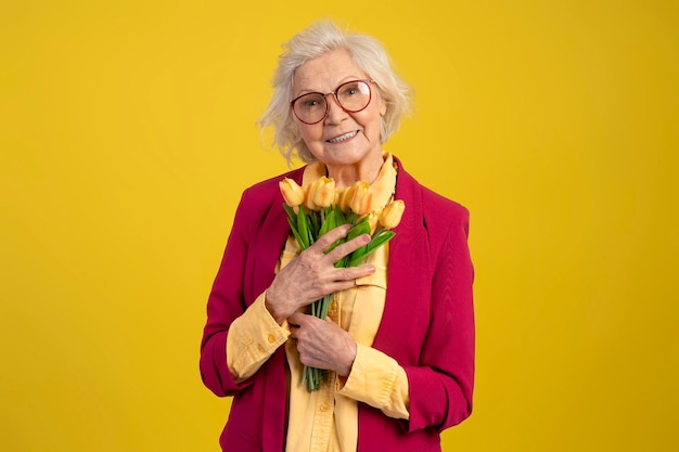 Grijze haren blanke vrouw met boeket gele tulpen camera kijken