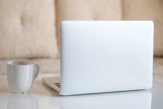 Grijze laptop met een witte mok op de tafel in de kamer. Thuiswerken. Detailopname.