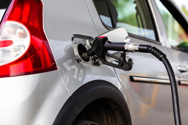 Grijze metalen auto tanken op tankstation close-up met selectieve aandacht en wazige man op achtergrond