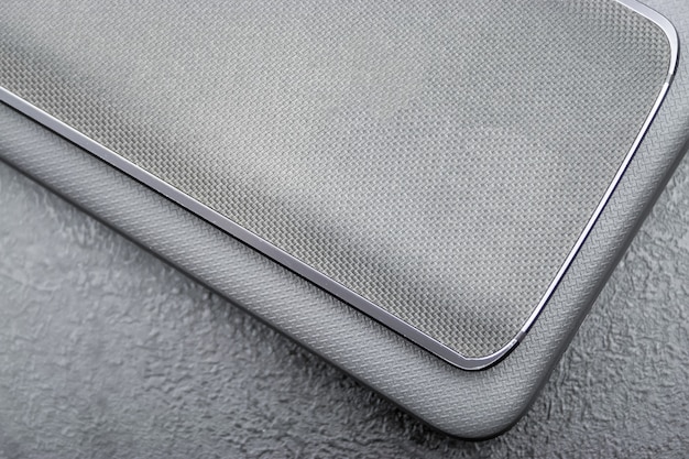 Grijze mobiele telefoon met een gebreide nylon achterkant ligt op een gesloten laptophoes met textuur op een grijze textuurachtergrond