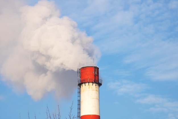 Grijze rook uit de schoorsteen van de plant in de blauwe lucht