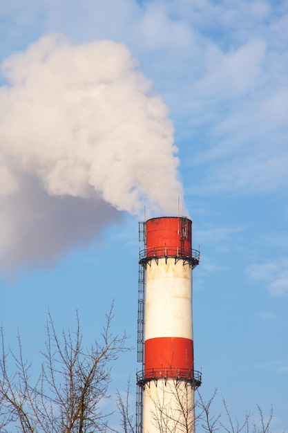 Grijze rook uit de schoorsteen van de plant in de blauwe lucht