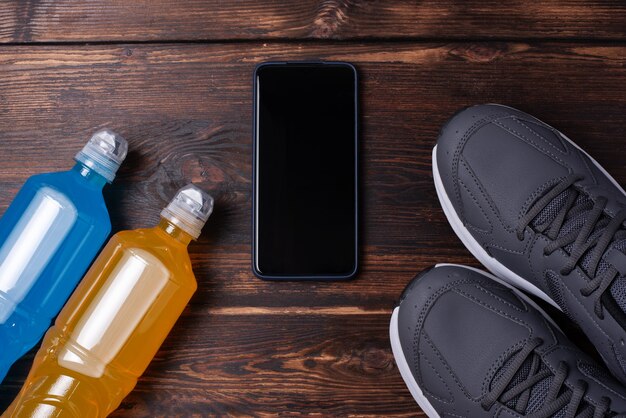 Grijze sneakers, smartphone en twee flessen isotone drank op een donkere houten achtergrond, mockup, sporttrainingsconcept, close-up.