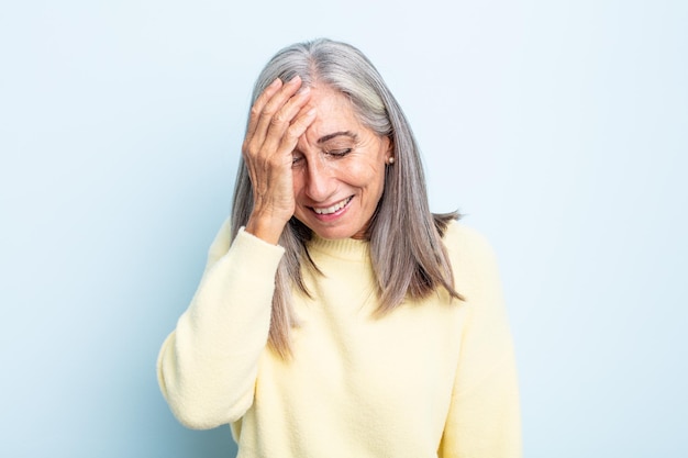 Grijze vrouw van middelbare leeftijd die lacht en op het voorhoofd slaat alsof ze d'oh zegt! Ik was het vergeten of dat was een stomme fout