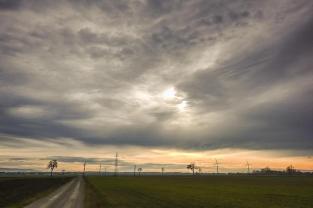 Grijze wolken aan de hemel met zon in een vlak landschap met windmolens