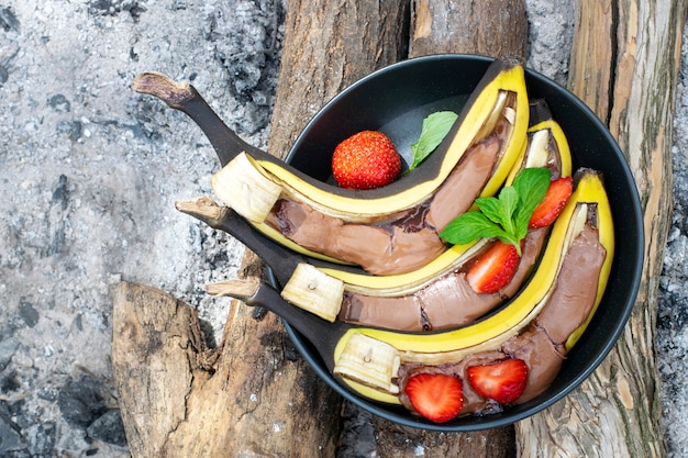 Grill banaan met chocolade. Picknick dessert idee. Zoete bananen in een plaat op houtskool. Bovenaanzicht.