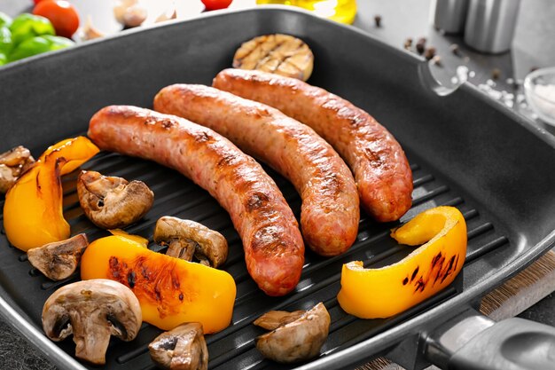 Photo grill pan with delicious sausages and vegetables closeup