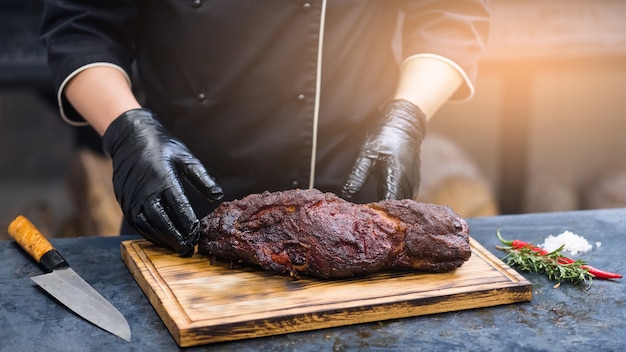 Grill restaurant kitchen. Closeup of chef hands in black cooking gloves serving smoked pork neck.