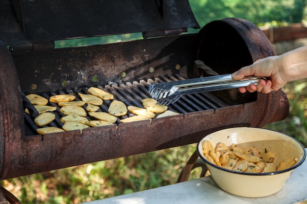 Foto le pinze per grill in mano mettono le patate su una griglia riscaldata