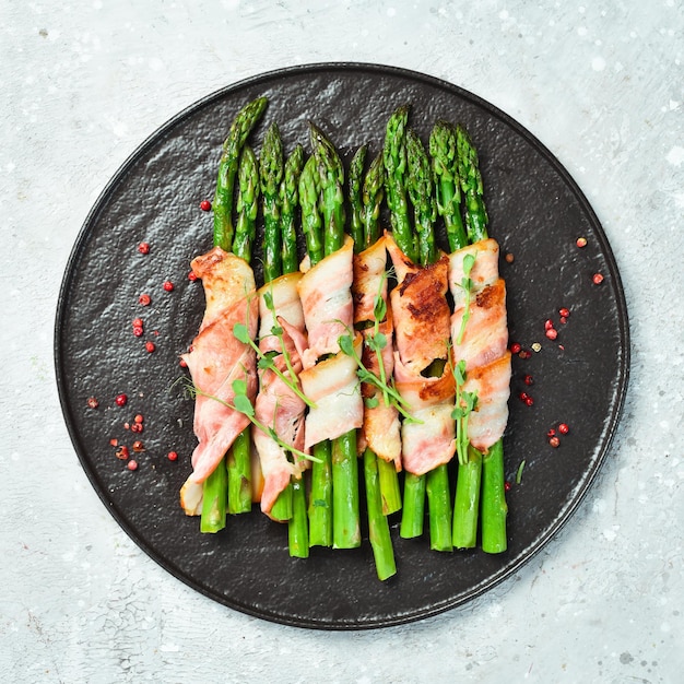 Grilled asparagus with bacon and basil on a plate On a stone background Top view