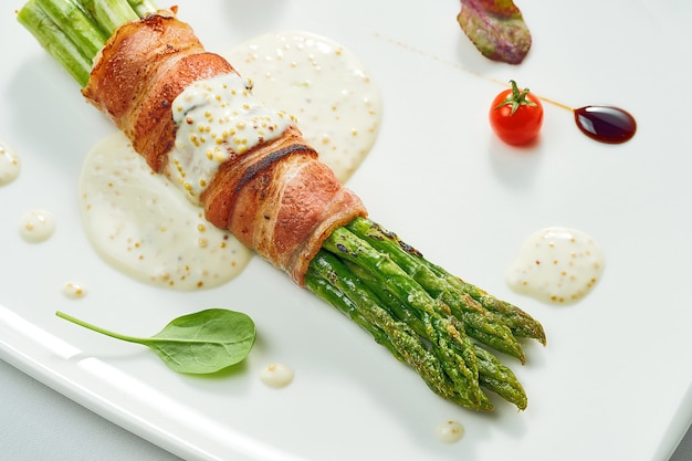 Asparagi alla griglia con pancetta e salsa di senape in un piatto bianco. isolato sulla superficie di gery.