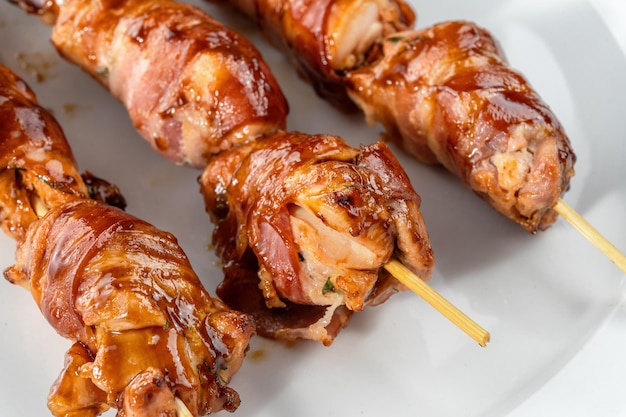 Grilled baconwrapped chicken tenders are laid out on a white
plate strung on wooden skewers macro