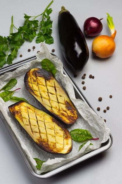 Grilled baked eggplants on pallet. Whole eggplant, onion and parsley on table.