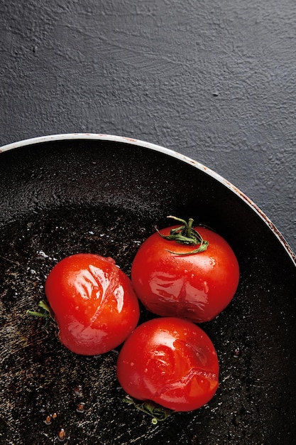 Grilled baked tomatoes in a black frying pan on a black concrete background