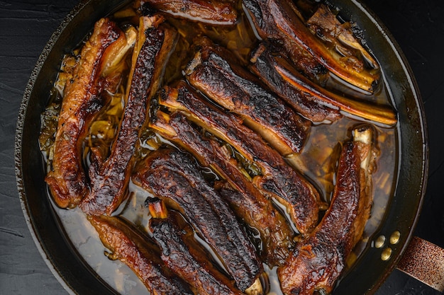 Grilled barbecue pork ribs set, in frying cast iron pan, on black stone table, top view flat lay