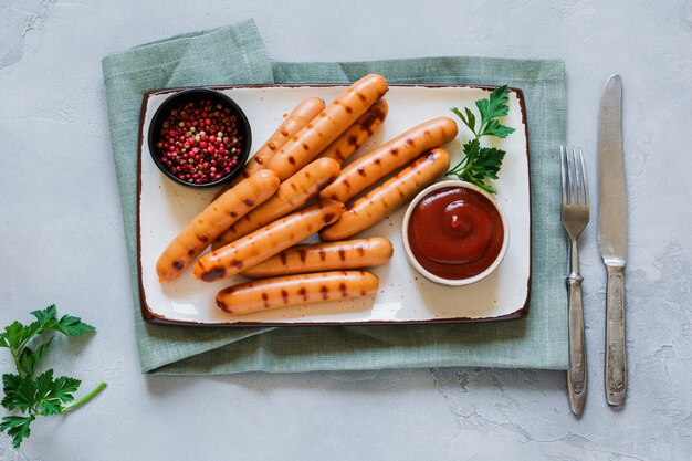 Grilled BBQ sausages with sauce and ketchup and garlic on ceramic plate on dark concrete table.