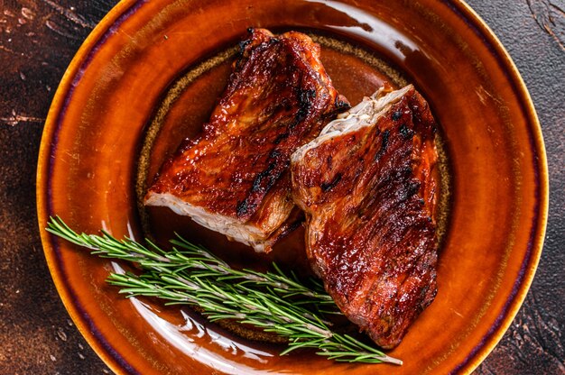 Grilled BBQ veal calf short spare rib meat on plate. Dark background. Top view.