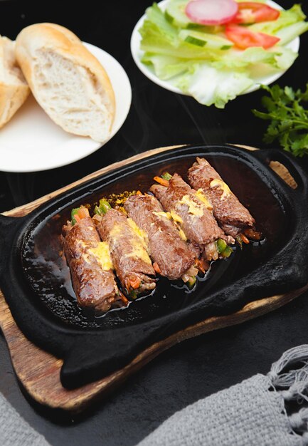 Grilled beef meat rolls with bell peppers, enoki mushrooms, carrots, salad, bread, bowls, and plates