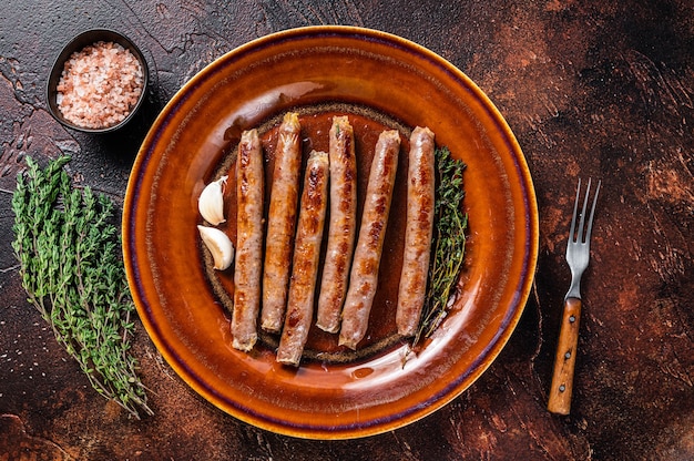 Grilled beef and pork meat sausage on rustic plate with thyme. Dark background. Top view.