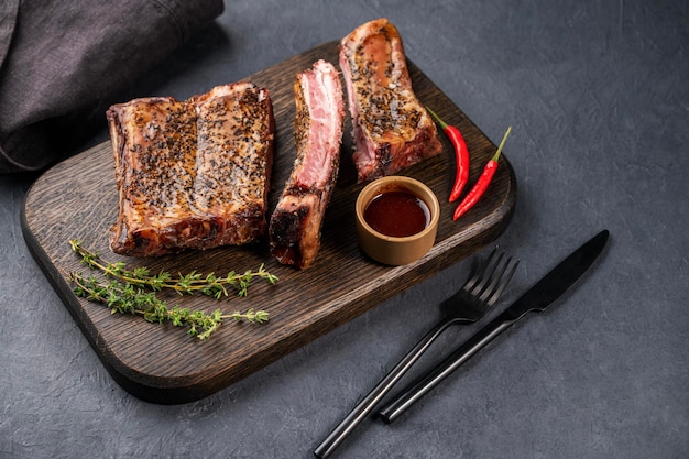 Grilled beef ribs with bbq sauce chili pepper and fresh herb on a wooden board on a dark background