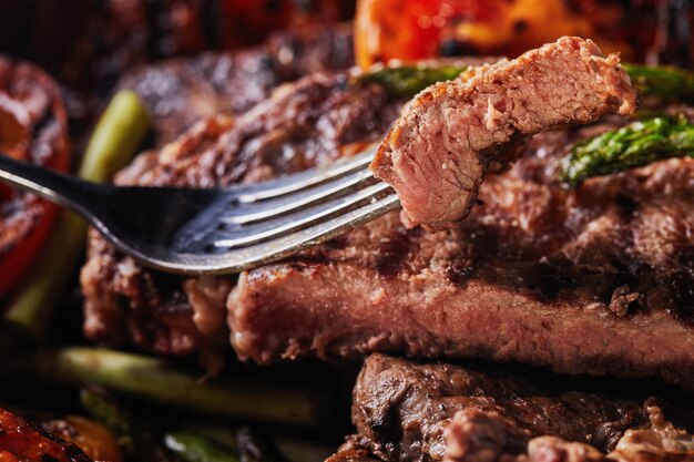 Grilled Beef steak in a black pan and a piece of chopped on a fork with baked vegetables