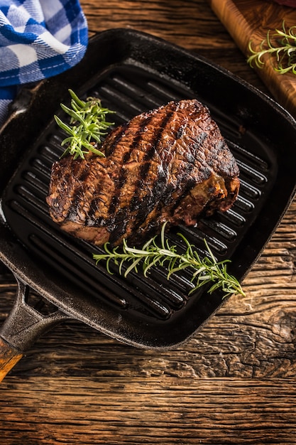 Grilled beef steak in grill pan with herbs rosemary on wooden table.