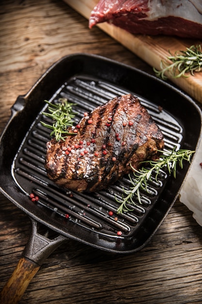 Grilled beef steak in grill pan with herbs rosemary on wooden table.