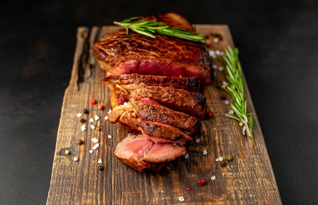 Grilled beef steak, herbs and spices on a cutting board on a stone background, top view