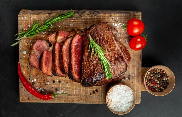 Grilled beef steak, herbs and spices on a cutting board on a stone background, top view