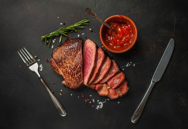 Grilled beef steak, herbs and spices on a stone background, top view