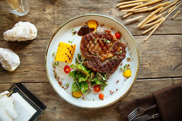 Grilled beef steak with corn on wooden surface