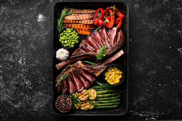 Grilled beef steak with grilled vegetables asparagus corn zucchini carrots and rosemary Tomahawk Top view Free copy space