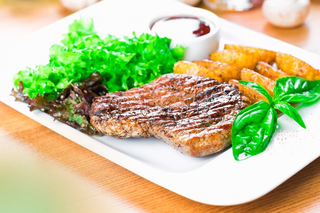 Grilled beef steak with potato wedges close up