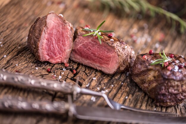 Grilled beef steak with rosemary, salt and pepper on old cutting board. Beef tenderloin steak.