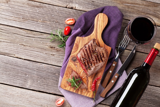 Grilled beef steak with rosemary, salt and pepper and wine bottle on wooden table. Top view with copy space