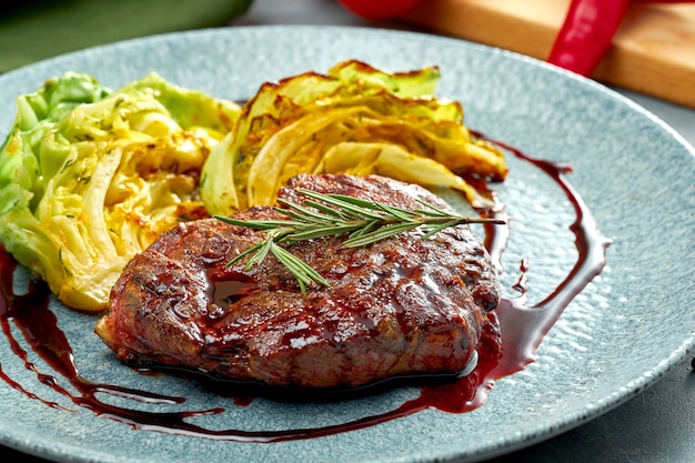 Grilled beef steak with a side dish of cabbage and sauce in a plate on a gray background