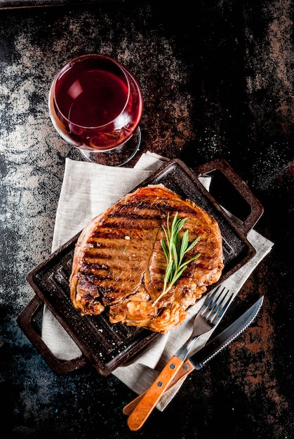 Photo grilled beef steak with spices on grill pan board, with and red wine glass.  copyspace top view