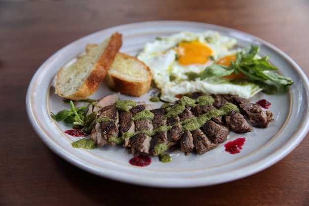 Grilled beef steak with toast , fried egg and vegetables on top with pesto sauce