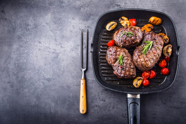 Grilled beef steaks in grilled pan with mushrooms tomatoes and rosemary.