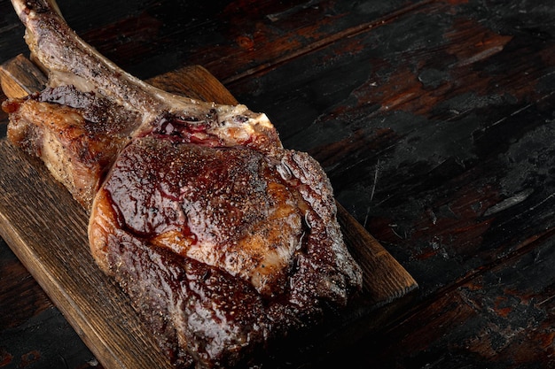 Grilled black angus beef tomahawk steak on bone set, on wooden serving board, on old dark  wooden table background, with copy space for text