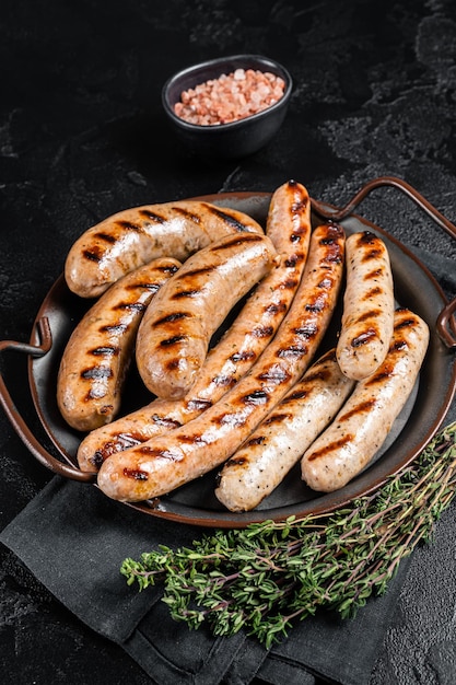 Grilled Bratwurst meat sausages on a steel tray with herbs Black background Top view