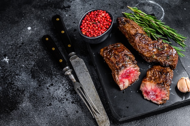 Grilled brisket steaks in bbq sauce on a marble board. Black background. Top view. Copy space.