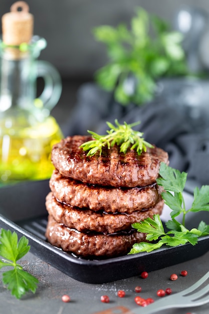 Grilled burger patties with herbs, spices on a dark