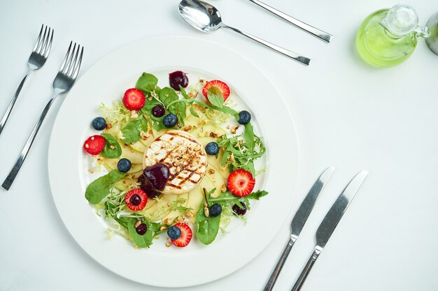 Grilled camembert cheese with apples, strawberries and blueberries in a white plate on white plate