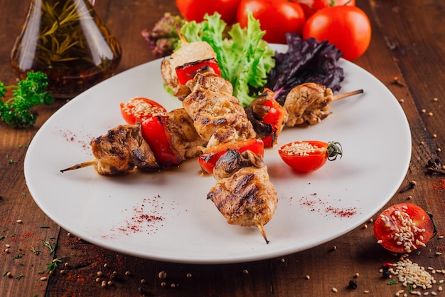 grilled chicken and bell pepper skewers with cherry tomatoes and spices on a white plate