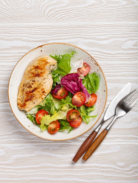 사진 신선한 토마토와 샐러드 잎을 곁들인 구운 닭 가슴살 필레 위에서 나무 배경의 하얀 접시, 건강한 저녁 식사 또는 다이어트 식사