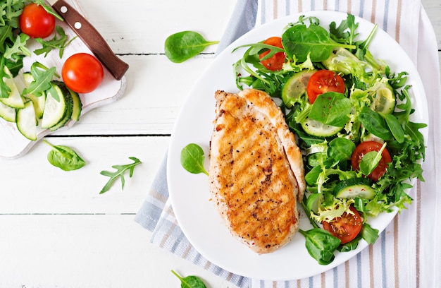 Grilled chicken breast and fresh vegetable salad - tomatoes, cucumbers and lettuce leaves. Chicken salad. Healthy food. Flat lay. 