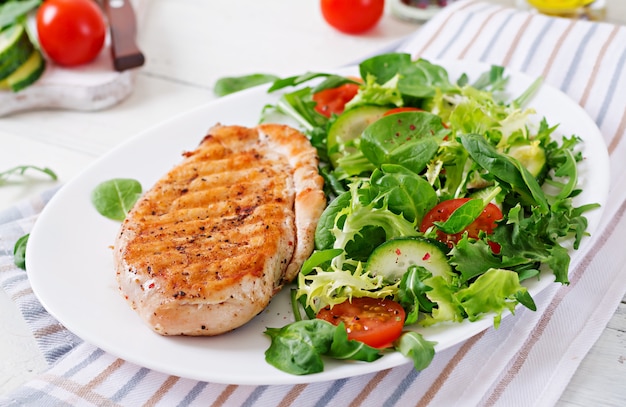 Grilled chicken breast and fresh vegetable salad - tomatoes, cucumbers and lettuce leaves. Chicken salad. Healthy food.